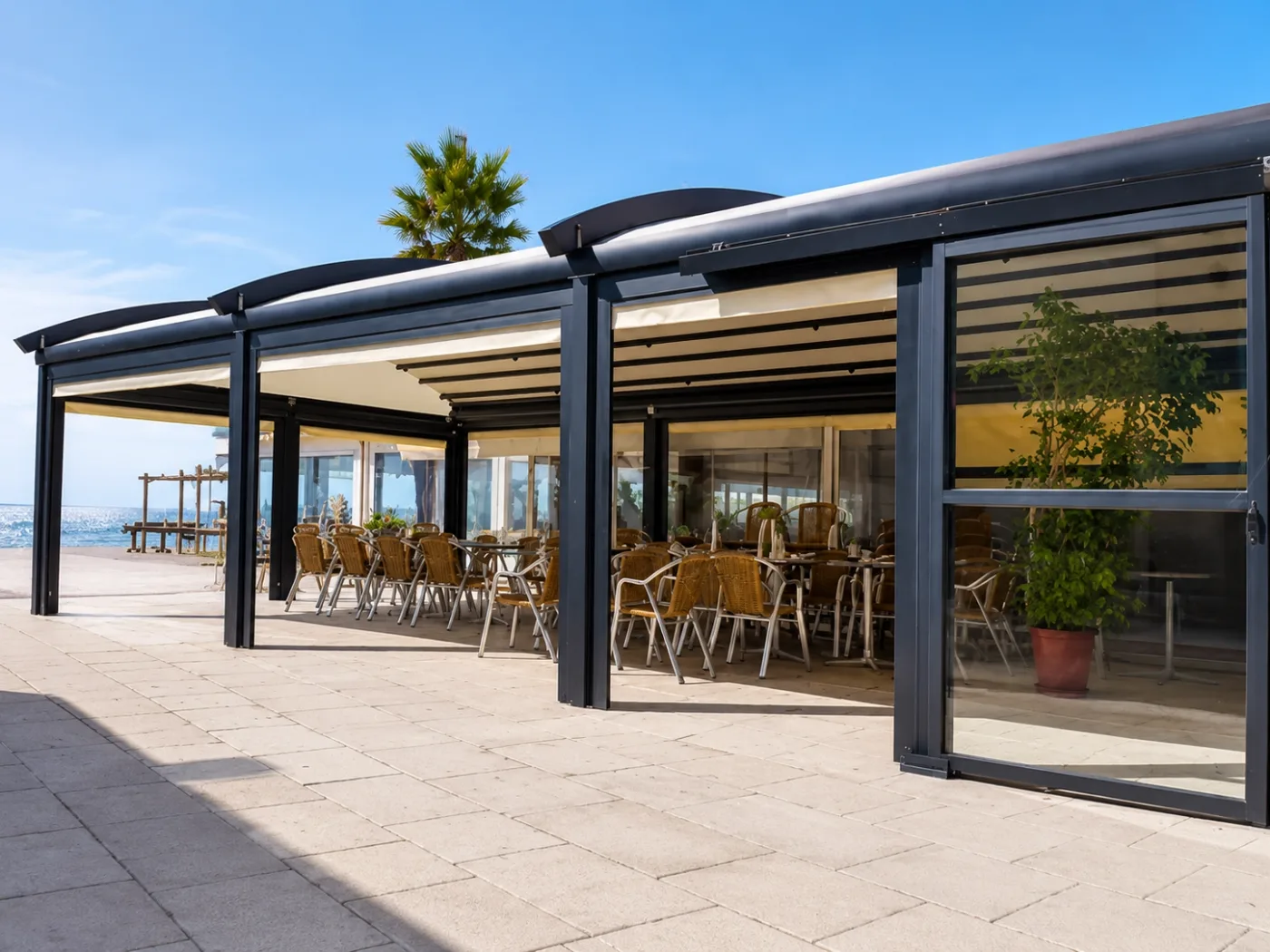Seaside hospitality terrace with curved awning roofs and vertical sliding glass elements