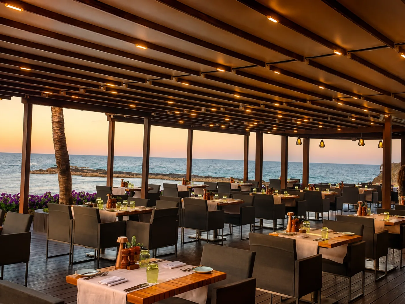 Seaside restaurant terrace under an illuminated pergola in evening light